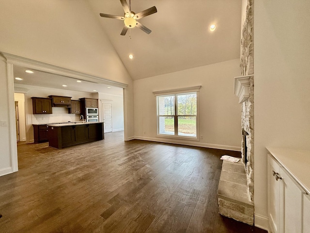 unfurnished living room featuring ceiling fan, sink, dark hardwood / wood-style flooring, high vaulted ceiling, and a fireplace