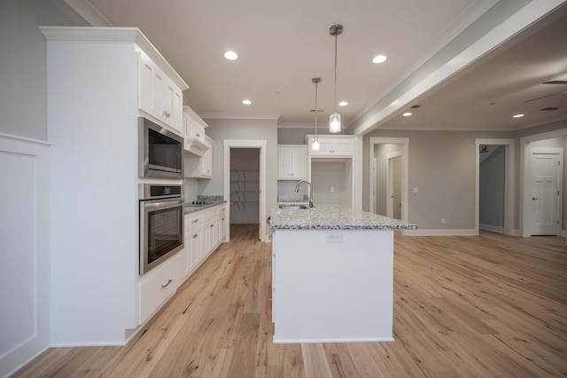 kitchen with white cabinets, stainless steel oven, an island with sink, and built in microwave