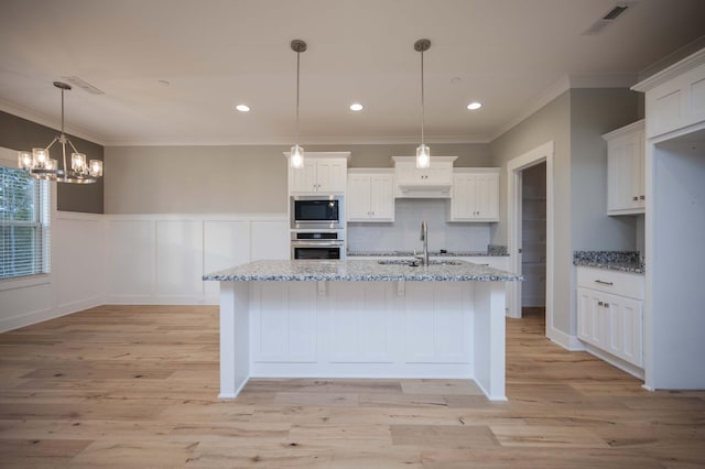 kitchen featuring white cabinetry, sink, light stone countertops, decorative light fixtures, and appliances with stainless steel finishes