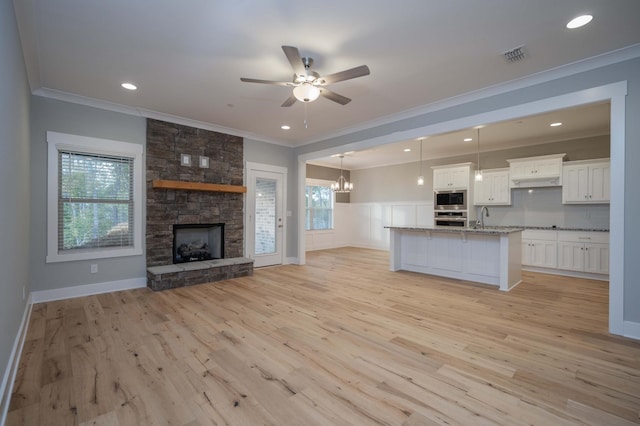 unfurnished living room featuring light hardwood / wood-style flooring, a stone fireplace, crown molding, and sink