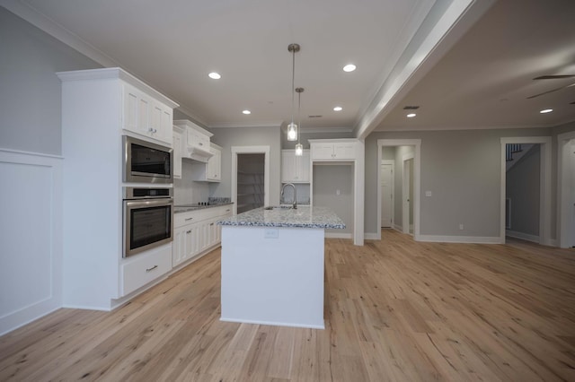 kitchen featuring white cabinets, appliances with stainless steel finishes, light stone countertops, and an island with sink