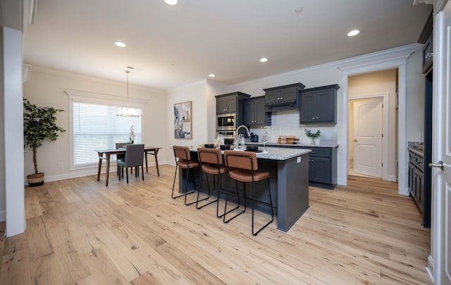 kitchen with a kitchen breakfast bar, light stone counters, light hardwood / wood-style floors, a center island with sink, and appliances with stainless steel finishes