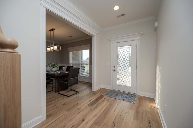 foyer entrance featuring light wood-type flooring, ornamental molding, and a chandelier