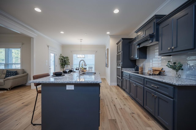 kitchen with black electric stovetop, sink, an island with sink, tasteful backsplash, and light hardwood / wood-style floors