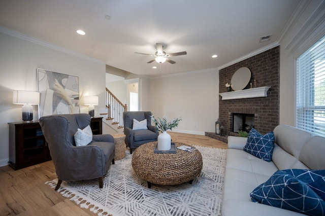 living room with hardwood / wood-style flooring, ceiling fan, ornamental molding, and a brick fireplace