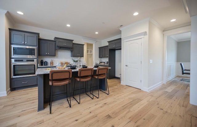 kitchen featuring crown molding, an island with sink, appliances with stainless steel finishes, light hardwood / wood-style floors, and a kitchen bar