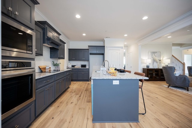 kitchen featuring a kitchen island with sink, crown molding, light hardwood / wood-style flooring, appliances with stainless steel finishes, and a kitchen bar