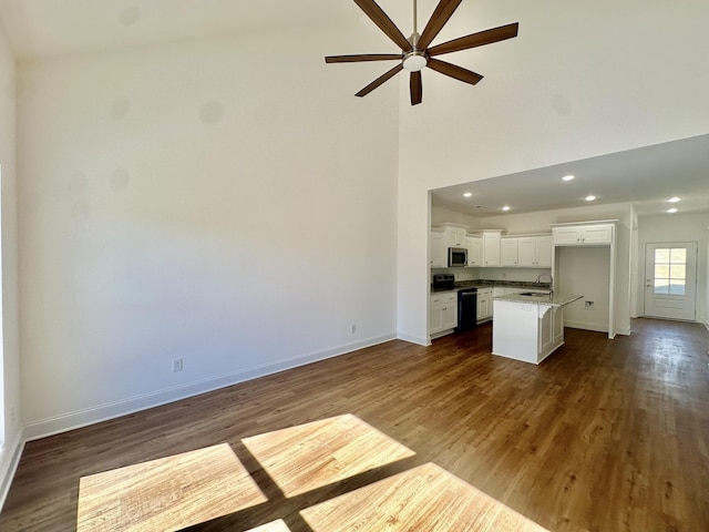 unfurnished living room with dark hardwood / wood-style flooring, ceiling fan, sink, and high vaulted ceiling