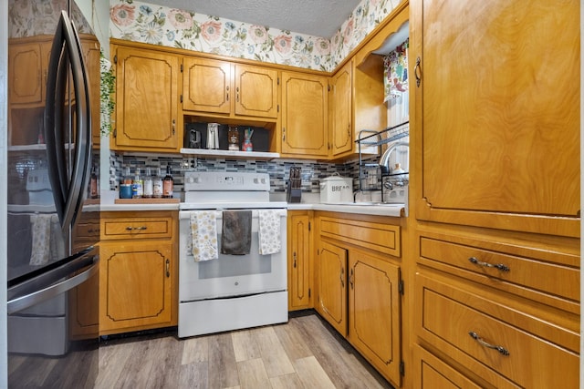 kitchen with electric range, sink, backsplash, refrigerator, and light wood-type flooring