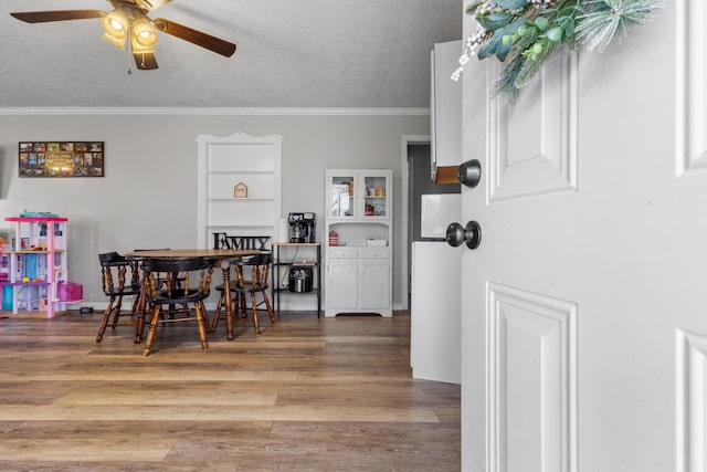 dining area with wood-type flooring, a textured ceiling, ceiling fan, and ornamental molding