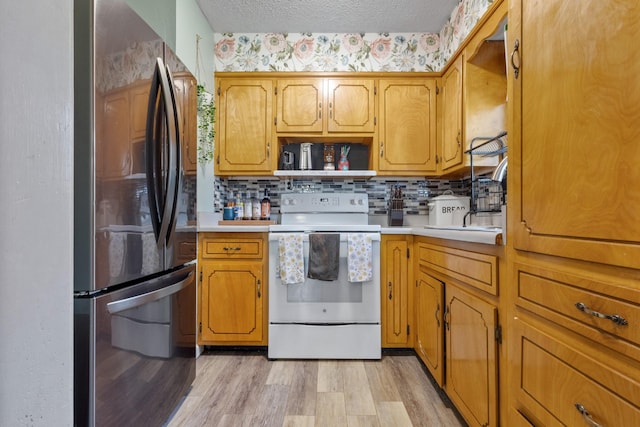 kitchen featuring white electric range oven, stainless steel fridge, light hardwood / wood-style floors, a textured ceiling, and decorative backsplash