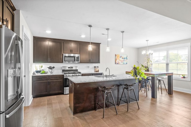 kitchen with pendant lighting, sink, light stone countertops, an island with sink, and stainless steel appliances