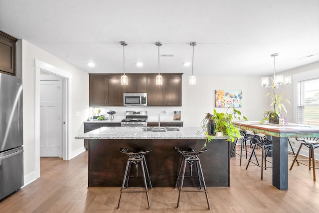 kitchen with sink, appliances with stainless steel finishes, an island with sink, dark brown cabinets, and light stone counters