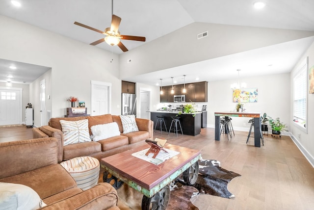 living room with ceiling fan with notable chandelier, lofted ceiling, and light hardwood / wood-style floors