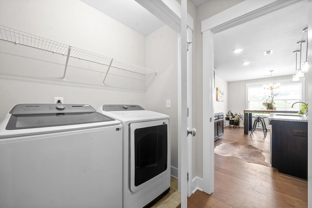 clothes washing area featuring washer and clothes dryer, a notable chandelier, sink, and light hardwood / wood-style floors