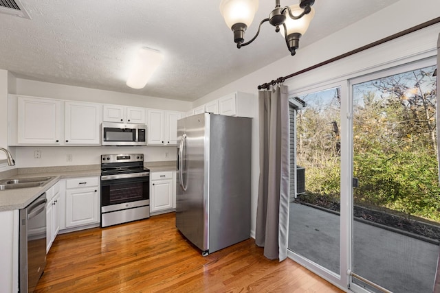 kitchen featuring appliances with stainless steel finishes, light wood-type flooring, sink, a chandelier, and white cabinetry