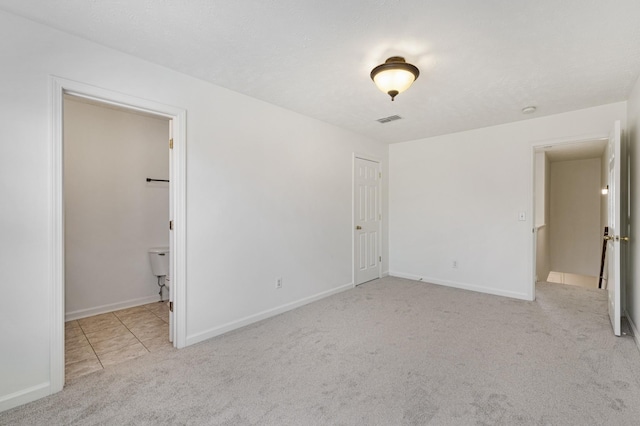 unfurnished bedroom with ensuite bathroom, light colored carpet, and a closet