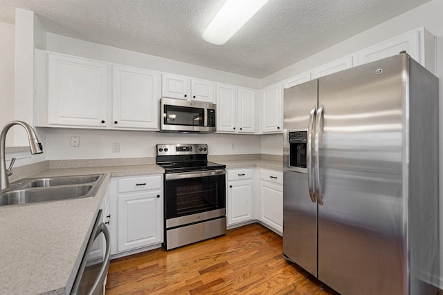 kitchen featuring a textured ceiling, stainless steel appliances, sink, light hardwood / wood-style flooring, and white cabinetry