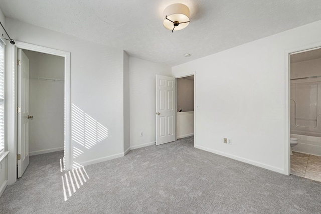 unfurnished bedroom featuring ensuite bathroom, light colored carpet, a walk in closet, and a closet