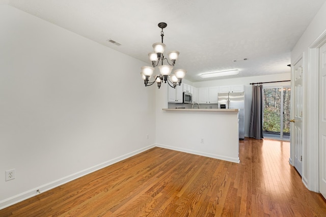 kitchen featuring light hardwood / wood-style flooring, a notable chandelier, kitchen peninsula, white cabinets, and appliances with stainless steel finishes