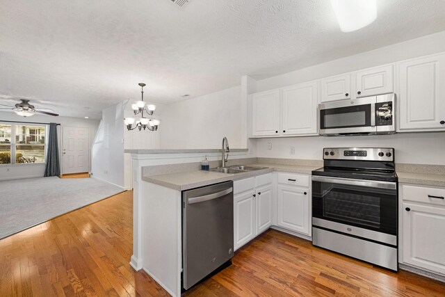 kitchen with kitchen peninsula, decorative light fixtures, stainless steel appliances, and white cabinetry