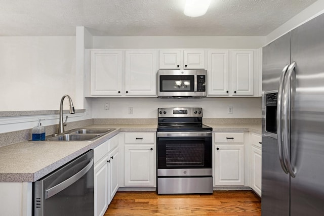 kitchen featuring white cabinetry, sink, a textured ceiling, appliances with stainless steel finishes, and hardwood / wood-style flooring