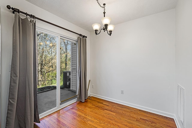 spare room featuring a chandelier, a textured ceiling, hardwood / wood-style flooring, and plenty of natural light