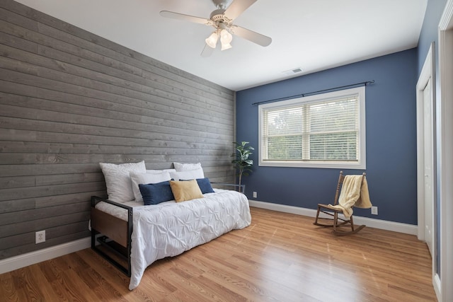 bedroom featuring hardwood / wood-style flooring, ceiling fan, and wood walls