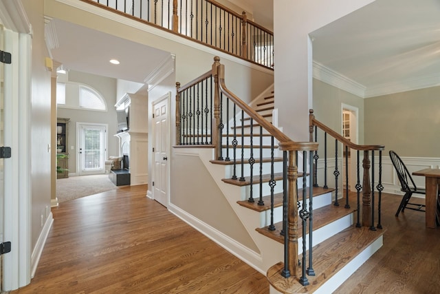 staircase featuring crown molding, wood-type flooring, and a high ceiling