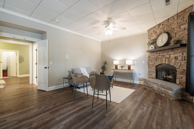 living room featuring ceiling fan, dark wood-type flooring, crown molding, a paneled ceiling, and a fireplace