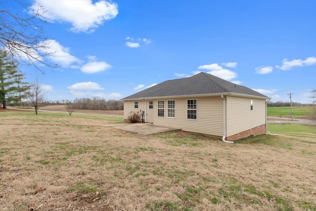 rear view of house featuring a rural view, a patio area, and a lawn