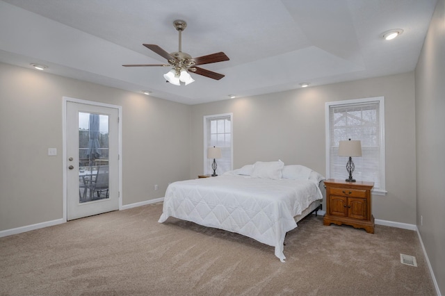 bedroom with access to exterior, ceiling fan, a raised ceiling, multiple windows, and light carpet