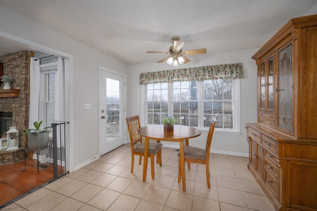 tiled dining space with a stone fireplace and ceiling fan