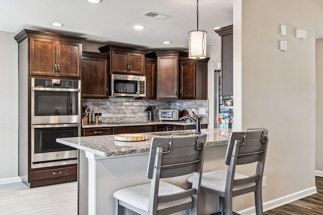 kitchen with pendant lighting, a kitchen breakfast bar, light stone countertops, and stainless steel appliances