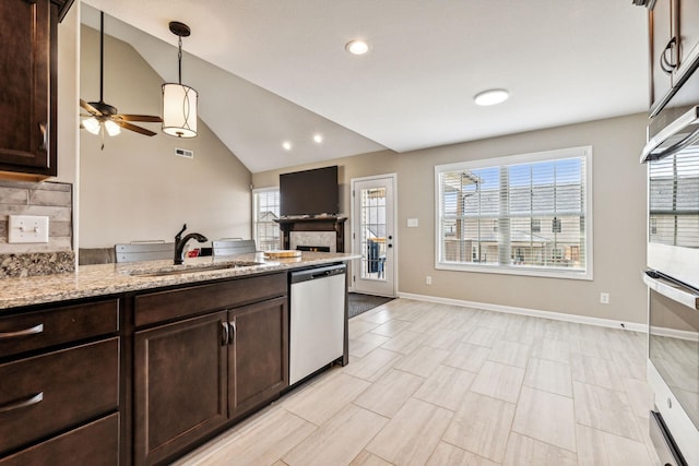 kitchen featuring light stone countertops, sink, hanging light fixtures, stainless steel appliances, and vaulted ceiling