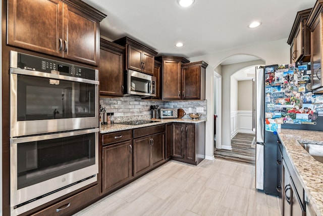 kitchen with light stone countertops, appliances with stainless steel finishes, and dark brown cabinetry