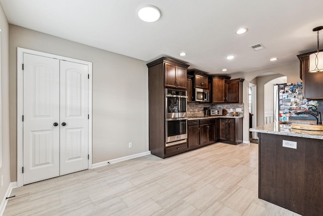 kitchen with appliances with stainless steel finishes, light stone counters, dark brown cabinets, sink, and hanging light fixtures