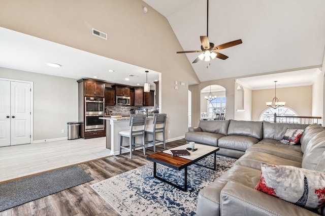 living room with high vaulted ceiling, light hardwood / wood-style floors, and ceiling fan with notable chandelier