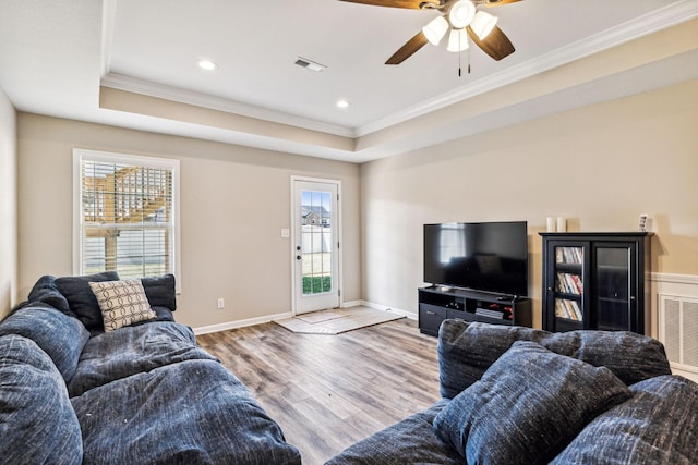 living room featuring light wood-type flooring, a raised ceiling, plenty of natural light, and ornamental molding