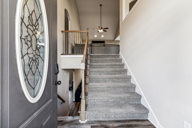 staircase with ceiling fan, hardwood / wood-style floors, and a high ceiling