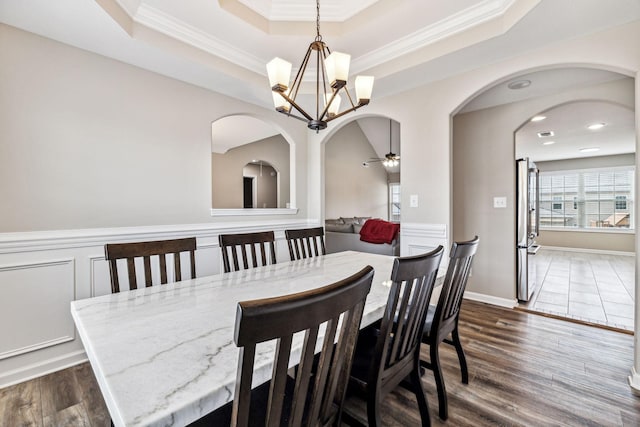 dining room with a raised ceiling, ceiling fan with notable chandelier, dark hardwood / wood-style floors, and ornamental molding