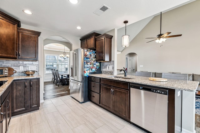 kitchen featuring backsplash, ceiling fan with notable chandelier, stainless steel appliances, dark brown cabinetry, and sink