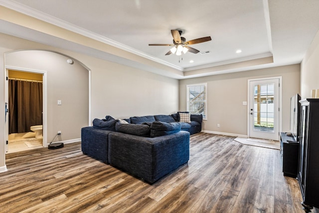 living room featuring ceiling fan, a raised ceiling, ornamental molding, and dark wood-type flooring