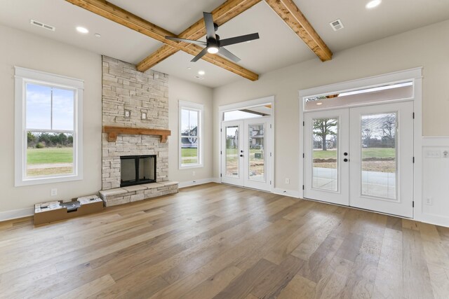 unfurnished living room with ceiling fan, french doors, a healthy amount of sunlight, a stone fireplace, and beamed ceiling