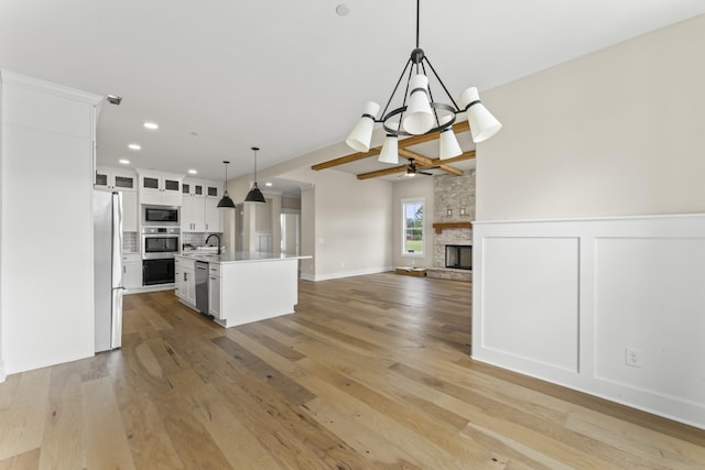 kitchen featuring stainless steel dishwasher, a kitchen island with sink, built in microwave, decorative light fixtures, and white cabinetry