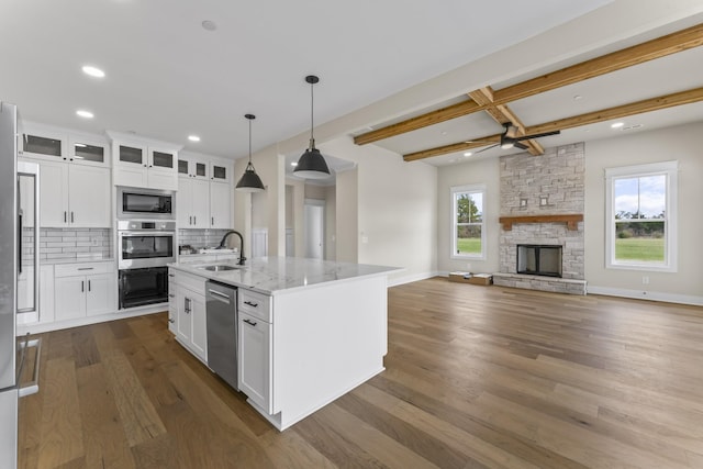 kitchen with backsplash, a center island with sink, light stone counters, white cabinetry, and stainless steel appliances