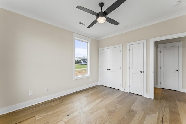 unfurnished bedroom featuring ornamental molding, light wood-type flooring, ceiling fan, and multiple closets