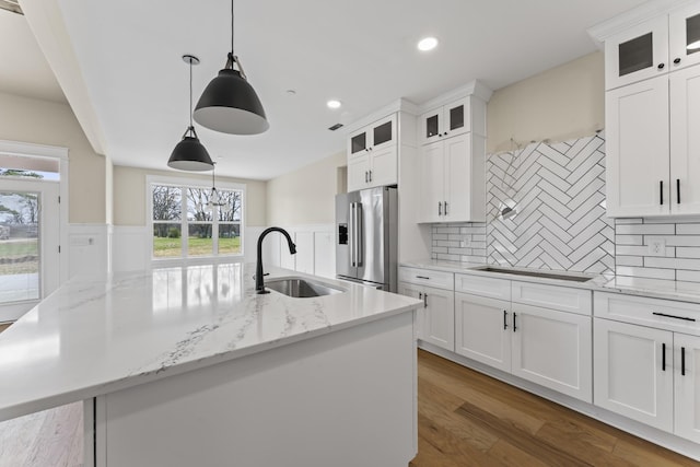 kitchen with white cabinetry, sink, stainless steel refrigerator with ice dispenser, decorative light fixtures, and a center island with sink