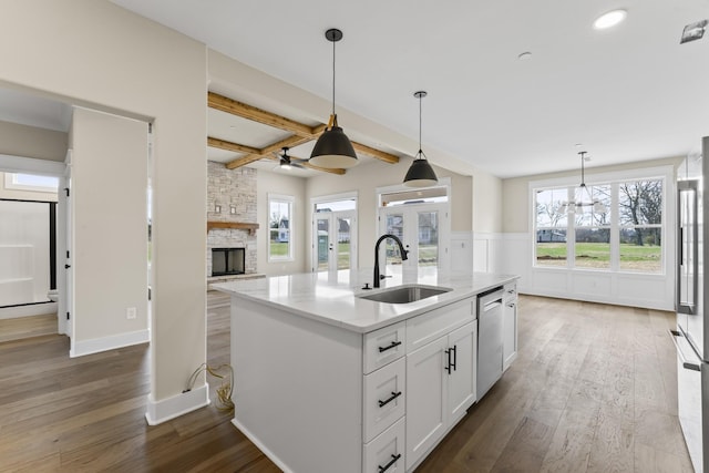 kitchen featuring sink, stainless steel appliances, beamed ceiling, an island with sink, and white cabinets