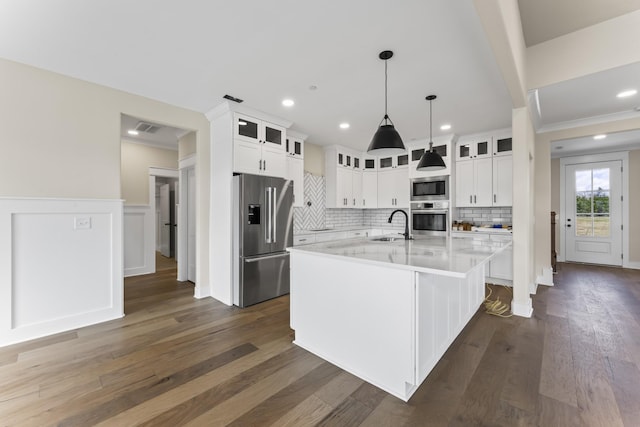 kitchen with a kitchen island with sink, white cabinets, sink, decorative light fixtures, and stainless steel appliances